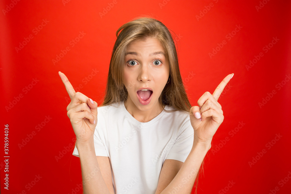 Pointing. Portrait of young caucasian woman with bright emotions on red studio background with copyspace. Blonde female model. Concept of human emotions, facial expression, sales, advertising, youth. Pointing. Portrait of young caucasian woman with bright emotions on red studio background with copyspace. Blonde female model. Concept of human emotions, facial expression, sales, advertising, youth.