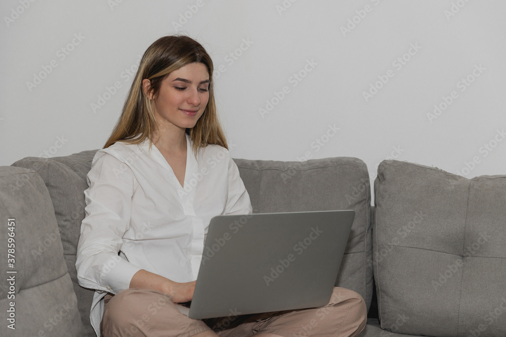 Young beautiful woman relaxing and cits on the sofa using laptop computer. Online chat. Working from home. Woman checking social apps. Online order food. Quarantine time. Freelancer and relax Young beautiful woman relaxing and cits on the sofa using laptop computer. Online chat. Working from home. Woman checking social apps. Online order food. Quarantine time. Freelancer and relax
