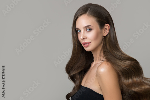 Portrait of young smiling brunette woman with makeup and hairstyle. Shiny wavy hair on gray background