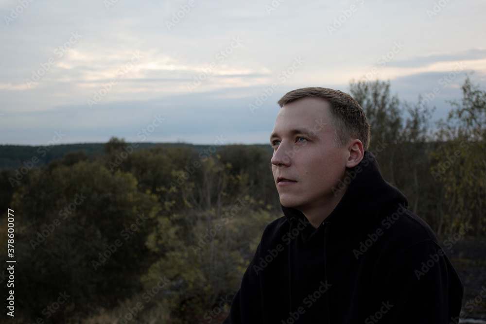 Portrait of a light guy in a black hoodie against the sky and forest. Blonde with blue eyes on top. Portrait of a light guy in a black hoodie against the sky and forest. Blonde with blue eyes on top.