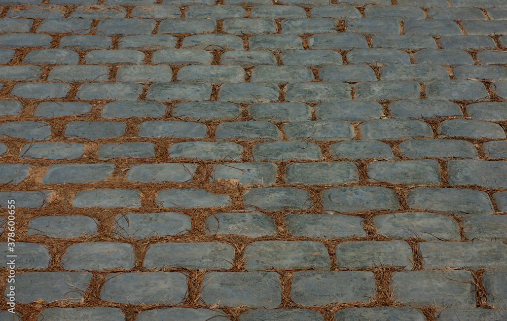 Blue cobblestone walk or street with dry grass between cobblestones. This is a closeup of an old sloped support system.