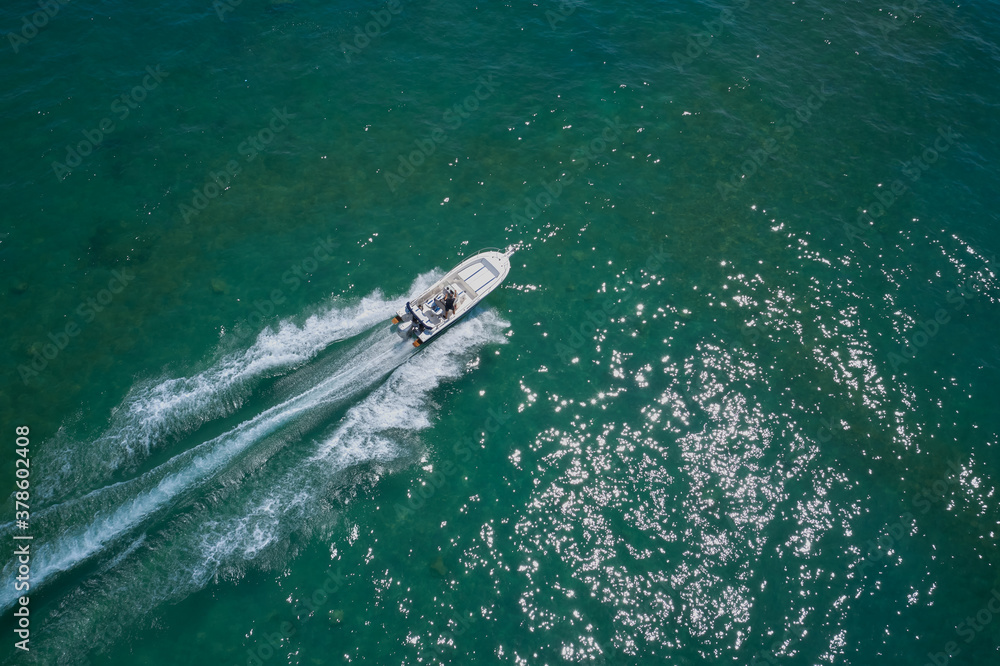 Drone view of a boat sailing. Top view of a white boat sailing to the blue sea. Motor boat in the sea. Travel - image. Drone view of a boat sailing. Top view of a white boat sailing to the blue sea. Motor boat in the sea. Travel - image.