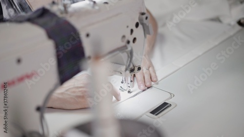 Female hands sew on a white sewing machine close-up. Concept of sewing in modern bright studio, woman sewing a white cloth, selective focus