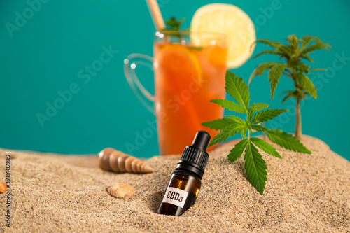 Product of CBDa oil, orangeade or ice tea in a jar and seashell on sand photo