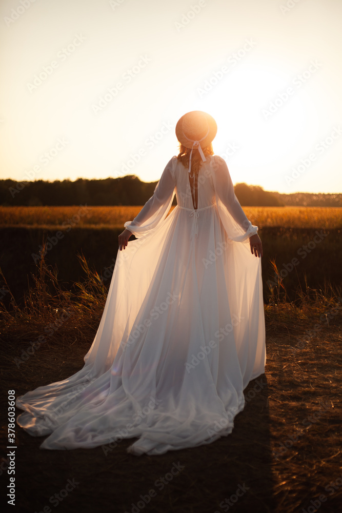 Happy woman standing with her back on sunset in nature .
Woman in a long white dress with a hat on her head Happy woman standing with her back on sunset in nature .
Woman in a long white dress with a hat on her head