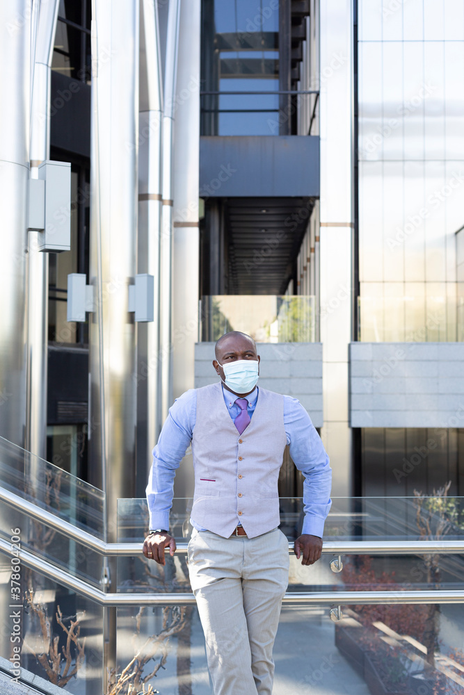 Black businessman in office building. He is pensive and wears a face mask. Space for text.