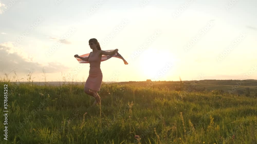 Young woman in pink summer dress walking on green field outdoors at sunset. Young woman in pink summer dress walking on green field outdoors at sunset.