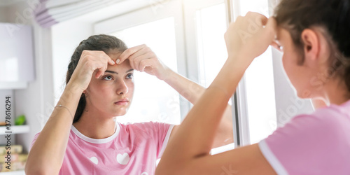 teenage girl in t-shirt pops pimples reflecting in mirror