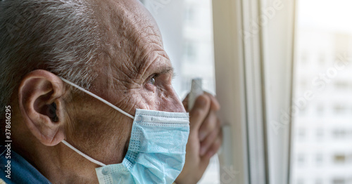 old man in blue disposable face mask looks through window