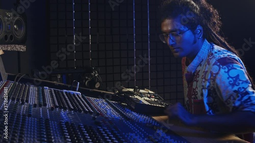 Music production. Male producer and dj. Hindi man working in the recording studio. An attractive brunette indian male person in a beautiful dress produces songs in headphones.  photo