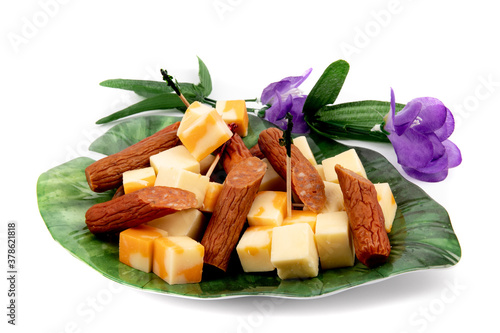 orange and white cheddar cheese cubes and pepperoni sausage chunks on a stylish leaf shaped plate and paper flowers on white photo