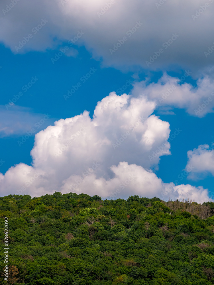 Massive cloud - towering cumulus - forming in the blue sky over hill with forest Massive cloud - towering cumulus - forming in the blue sky over hill with forest