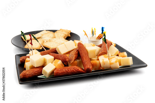 a modern square black plate of orange and white cheddar cheese cubes and pepperoni sausage chunks and a plate of wheat crackers on white photo