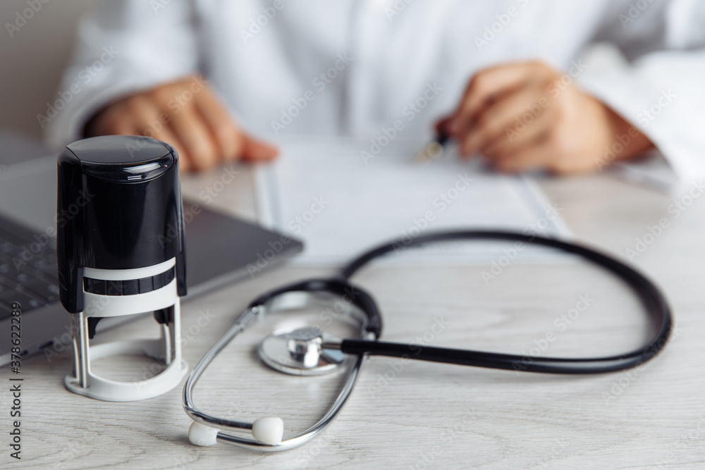 Doctor is signing medical document in office. Stethoscope and stamp on wooden table. Healthcare concept. Doctor is signing medical document in office. Stethoscope and stamp on wooden table. Healthcare concept.