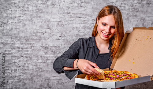 portrait of young teenager brunette girl with long hair with box of pizza on gray wall background