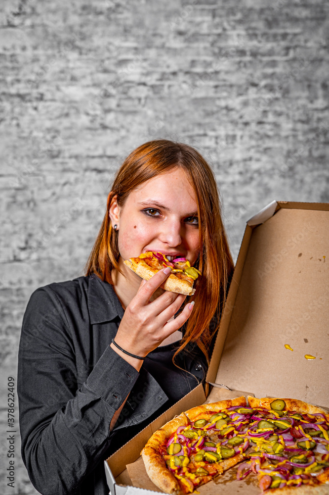portrait of young teenager brunette girl with long hair with box of pizza on gray wall background
