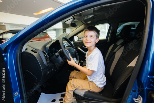 In a car dealership, a happy boy is driving a new car. Car purchase