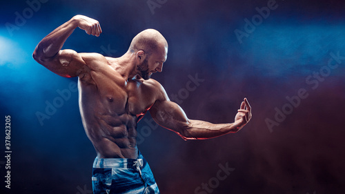 Handsome strong bodybuilder posing in studio on black background with smoke.