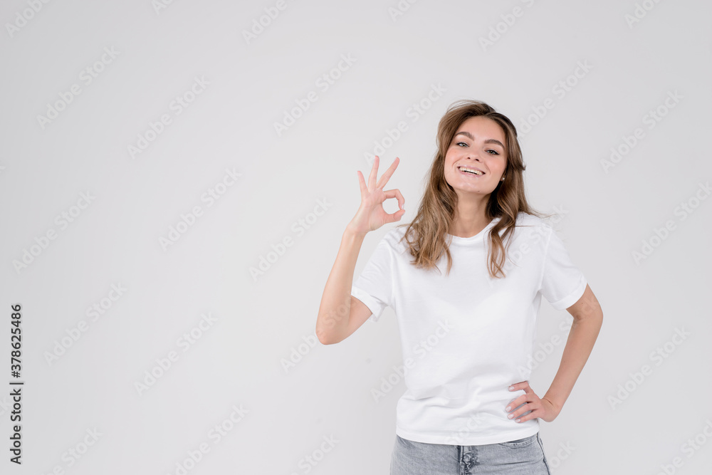 Portrait of a young smiling woman showing okey gesture sign, satisfied female client recommends service or product, looking at camera, isolated on white grey studio background, empty space Portrait of a young smiling woman showing okey gesture sign, satisfied female client recommends service or product, looking at camera, isolated on white grey studio background, empty space