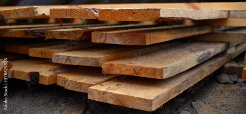 New brown boards are neatly stacked to dry. Lumber of second grade (with presence of bark) is numbered at ends, side view, close-up. There are traces of mold from moisture and water.