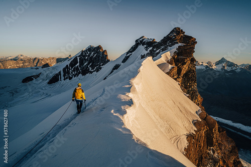 Murais de parede An alpinist climbing a rocky and snow mountain ridge during sunrise