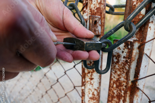 A male hand unlocks a lock on a rusty gate from an old fence