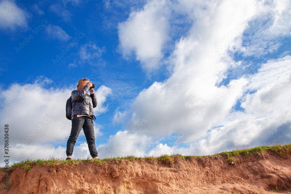 a tourist girl with a backpack and a camera walks along the river Bank on a Sunny day, taking pictures of the landscape, autumn