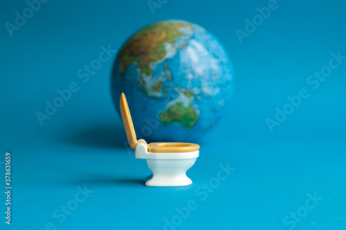 White toilet with an orange lid on a blue background with a globe in honor of world toilet day 19 November which is dedicated to public toilets and their maintenance