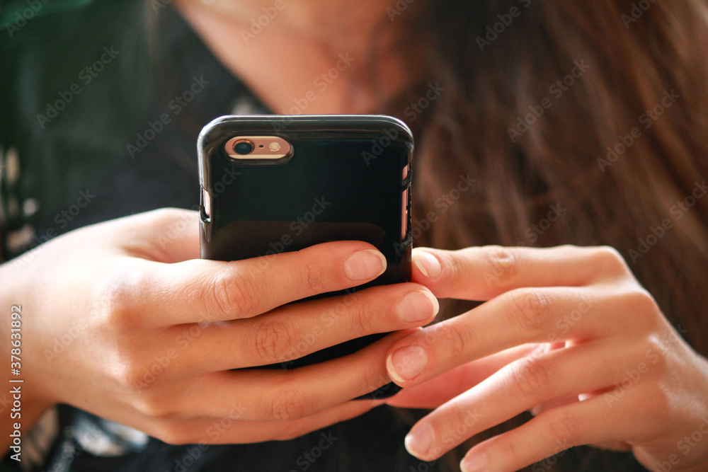 Młoda kobieta trzymająca w dłoniach smartfon w czarnym etui - obrazy, fototapety, plakaty 