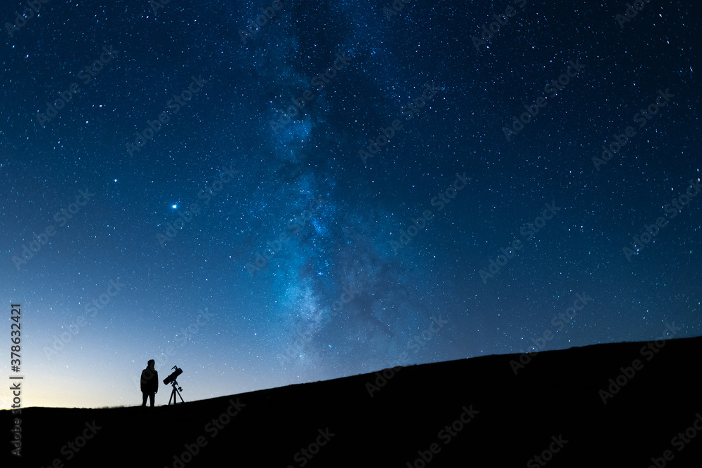 Person observing the blue starry sky with a telescope at night. Silhouette of an astronomer observing the immensity of the universe and the Milky Way