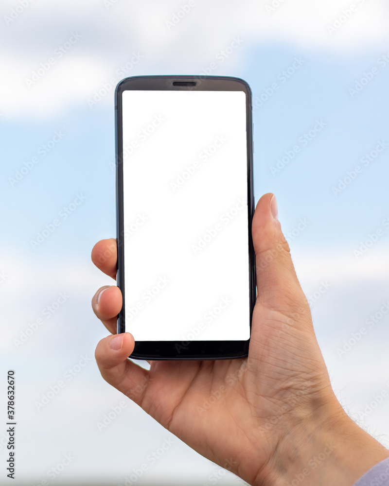Hand with the phone upright against the blue sky. Smartphone with a white screen, copy space.