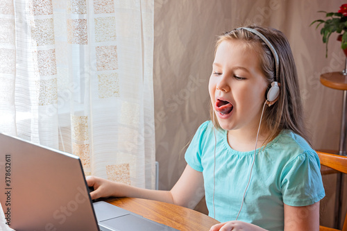 Speech training concept. Little girl uses a laptop to study at home with a teacher, a speech therapist. Distance learning. A kid doing exercises for correct pronunciation. photo