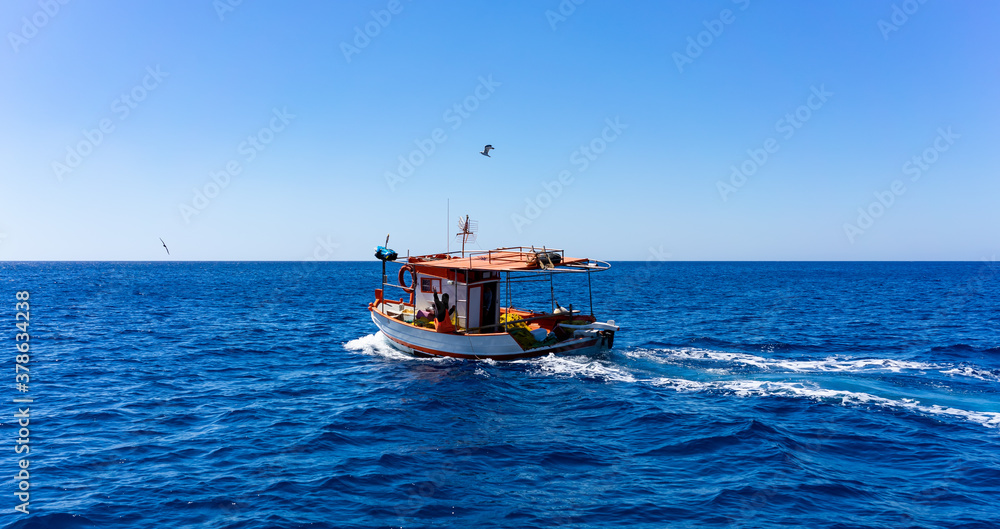 Orange and white fishing boat followed by seagulls on aegean sea. blue sky and sunny day