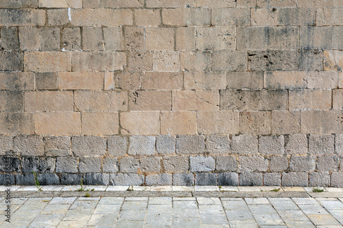 Exterior detail of an old Mediterranean historic building, stone wall facade and street.