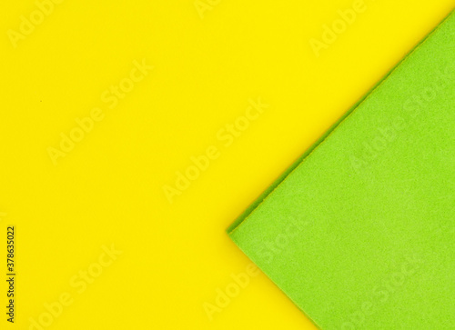 Green microfiber and green kitchen gloves on a light yellow background, top view.