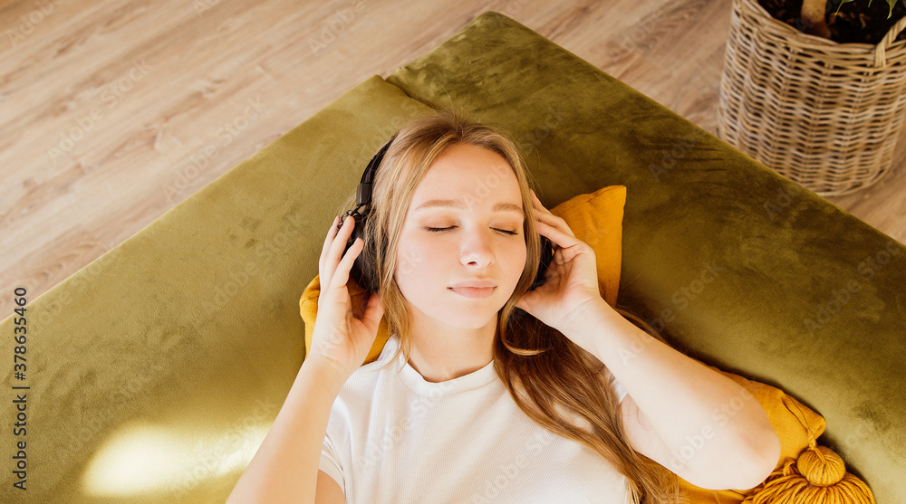 Calm young woman enjoys listening chill music audio sound meditating feeling no stress at home. Student female relaxing on bed with closed eyes and wearing headphones. 