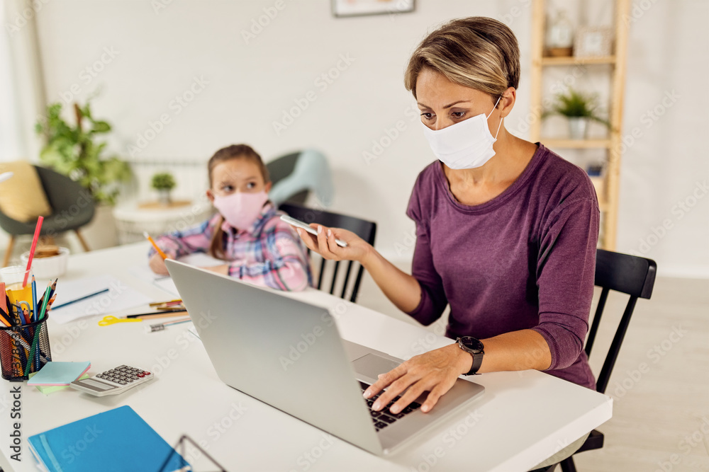 Young mother with face mask working on laptop at home due to coronavirus epidemic. Young mother with face mask working on laptop at home due to coronavirus epidemic.