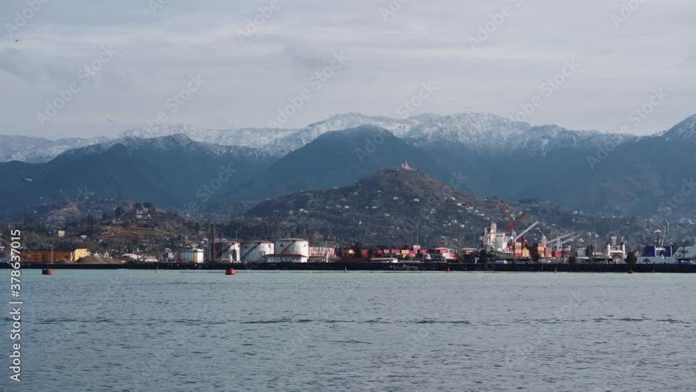 Port on the shore of the strait. Large mountains and strong waves of the sea in cloudy weather. Beautiful landscape in Georgia.
