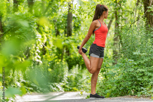 Fit stretch woman stretching quad leg muscle standing getting ready to run jogging outside in summer nature forest park green trees background. Fitness runner athlete running girl.