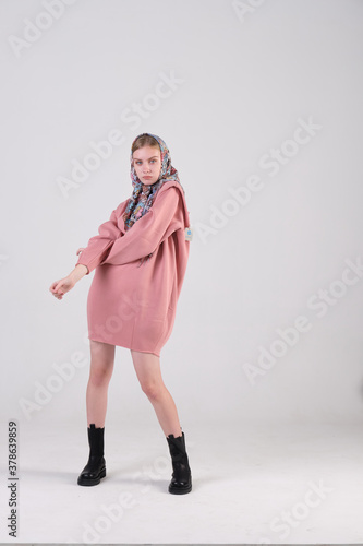 Russian young fashion model wearing ethnic shawl on her head and pink oversized dress posing in studio cyclorama.