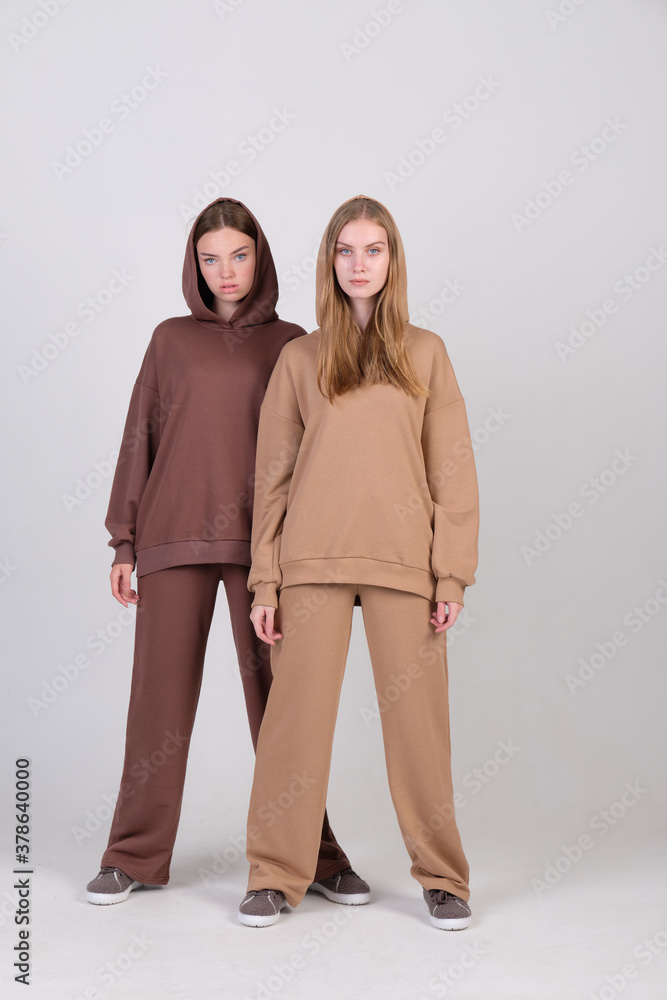 Pair of fashionable models posing in studio in brown and beige casual suits for clothing catalog. Examples of autumn female fashion. Pair of fashionable models posing in studio in brown and beige casual suits for clothing catalog. Examples of autumn female fashion.