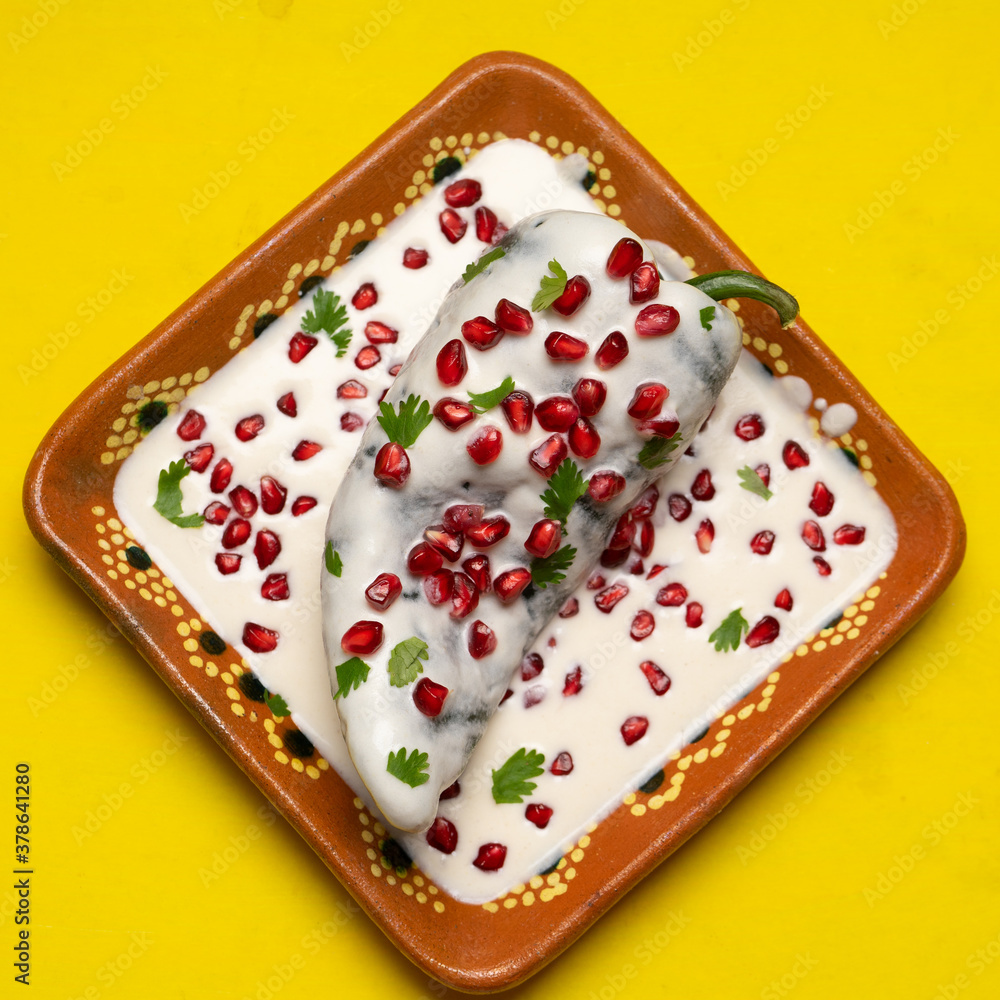 Mexican stuffed poblano peppers also called nogada with pomegranate on yellow background