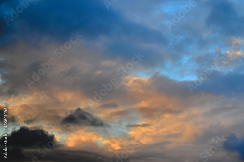 Fototapeta Naklejka Na Ścianę i Meble -  tufts of clouds shaded with gray and orange covering a twilight blue sky.