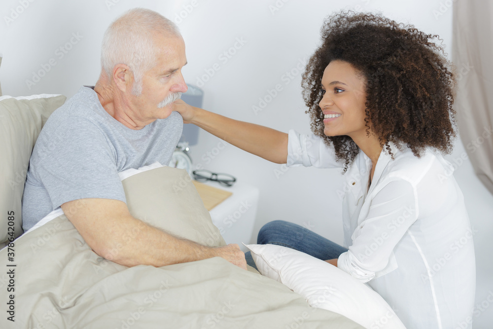 young lady reassuring elderly man in bed young lady reassuring elderly man in bed