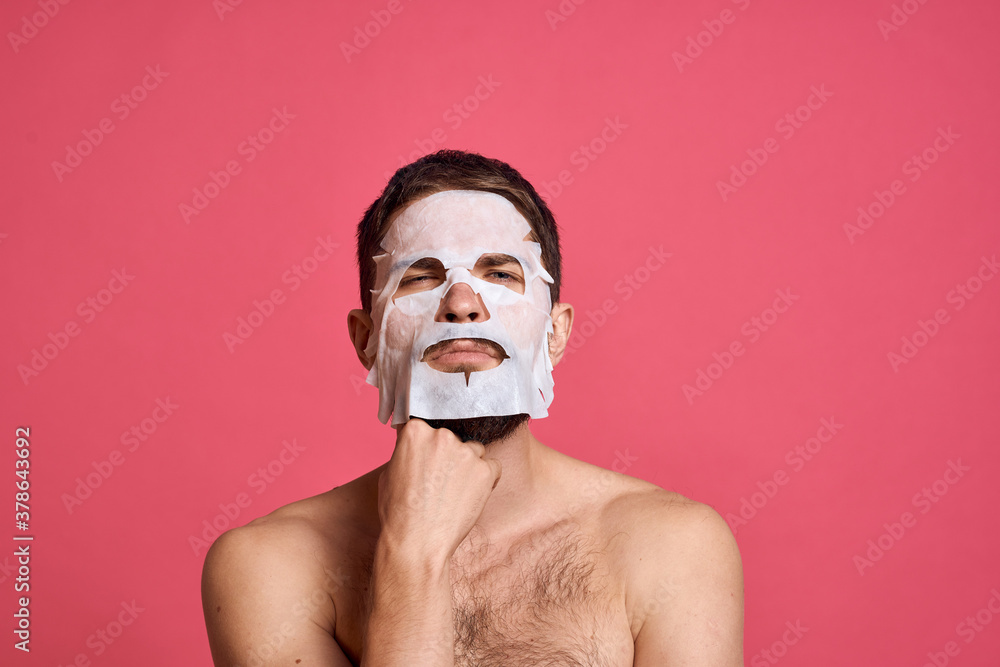 Fototapeta premium Man with bare shoulders in a white mask clear skin pink background