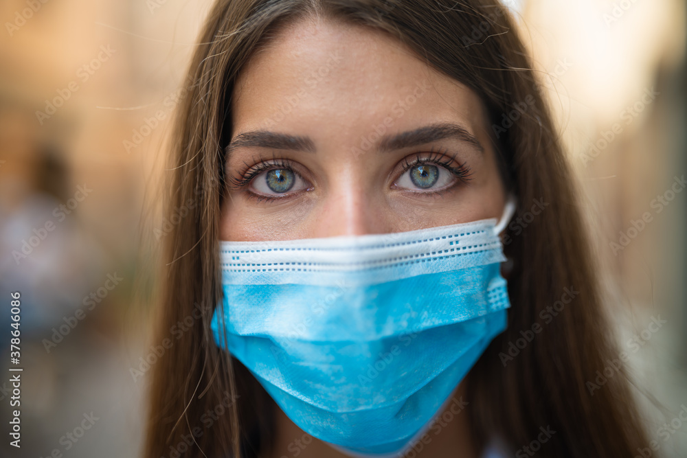 Authentic close up shot of an young woman is wearing a medical mask to protect herself from disease and looking in camera while taking a walk in old city center.