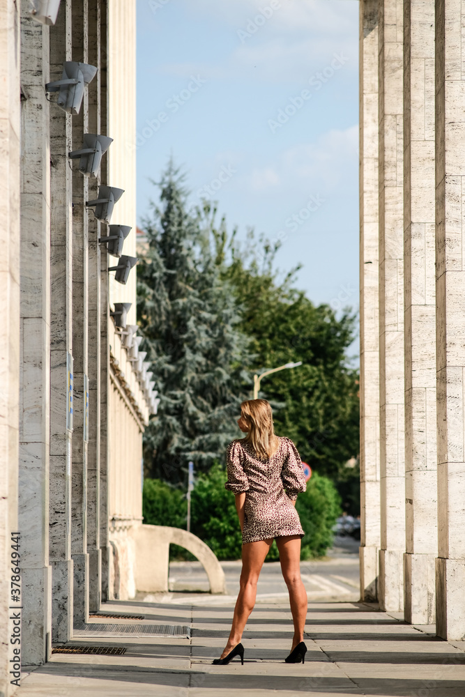 Fototapeta premium A blonde girl in a leopard dress poses candidly in a deserted city. Empty streets