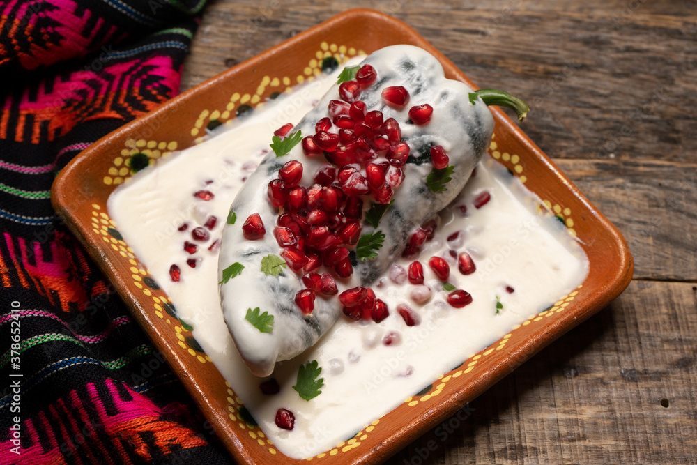 Mexican stuffed poblano peppers also called nogada with pomegranate on wooden background