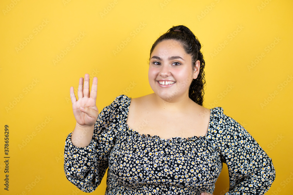Young beautiful woman with curly hair over isolated yellow background showing and pointing up with fingers number four while smiling confident and happy Young beautiful woman with curly hair over isolated yellow background showing and pointing up with fingers number four while smiling confident and happy