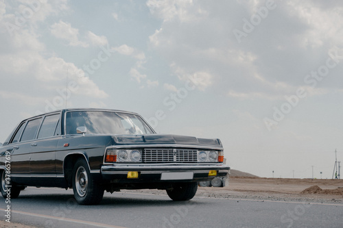Fototapeta Naklejka Na Ścianę i Meble -  Black luxury retro car.Soviet retro car close up.retro car in black color at the minimalistic background of desert terrain and blue sky.
